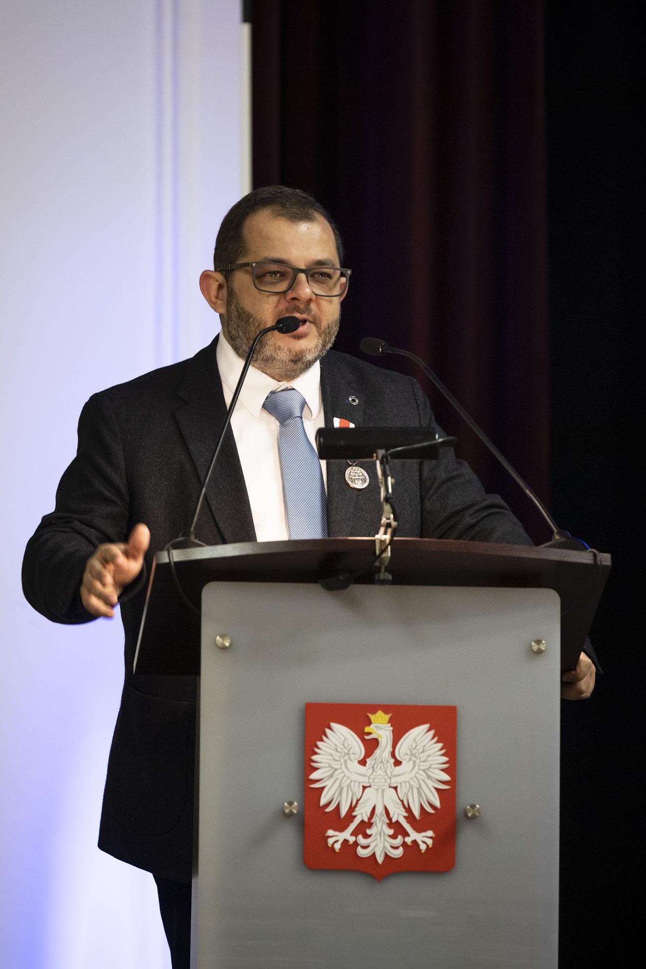 Profesor Tomasz Grzyb stojący przy mównicy. Z przodu mównicy widać logo Polski.