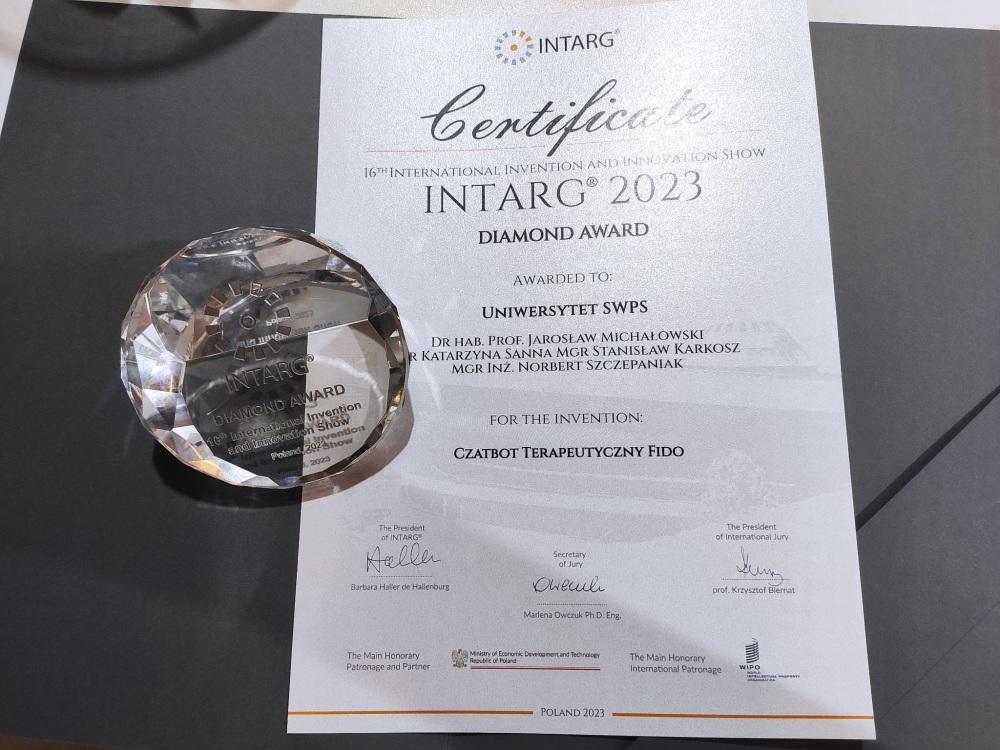 Zdjęcie certyfikatu „Diamond Award” dla Uniwersytetu SWPS za chatbota terapeutycznego Fido. Na certyfikacie leży diament z napisami