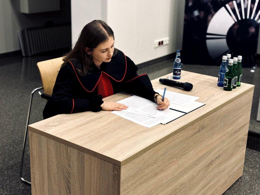 Młoda kobieta w todze prokuratorskiej pisze na kartce