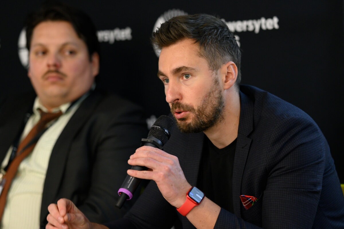 Michał Nowakowski bierze udział w debacie dotyczącej jakości życia, która odbywa się na Uniwersytecie SWPS; na drugim planie siedzi David Campos
