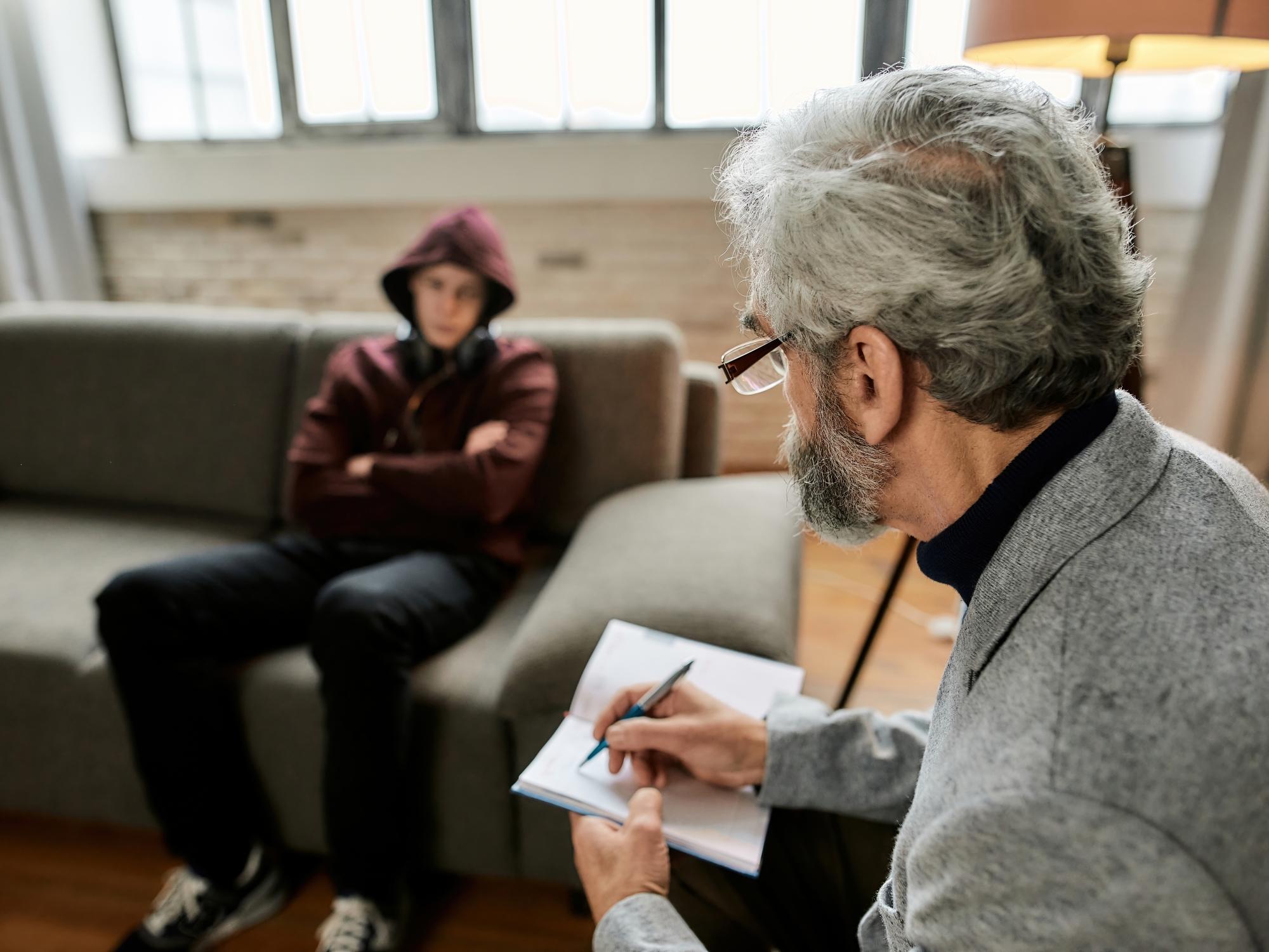 Nastolatek podczas wizyty u psychoterapeuty, siedzi w kapturze na kanapie