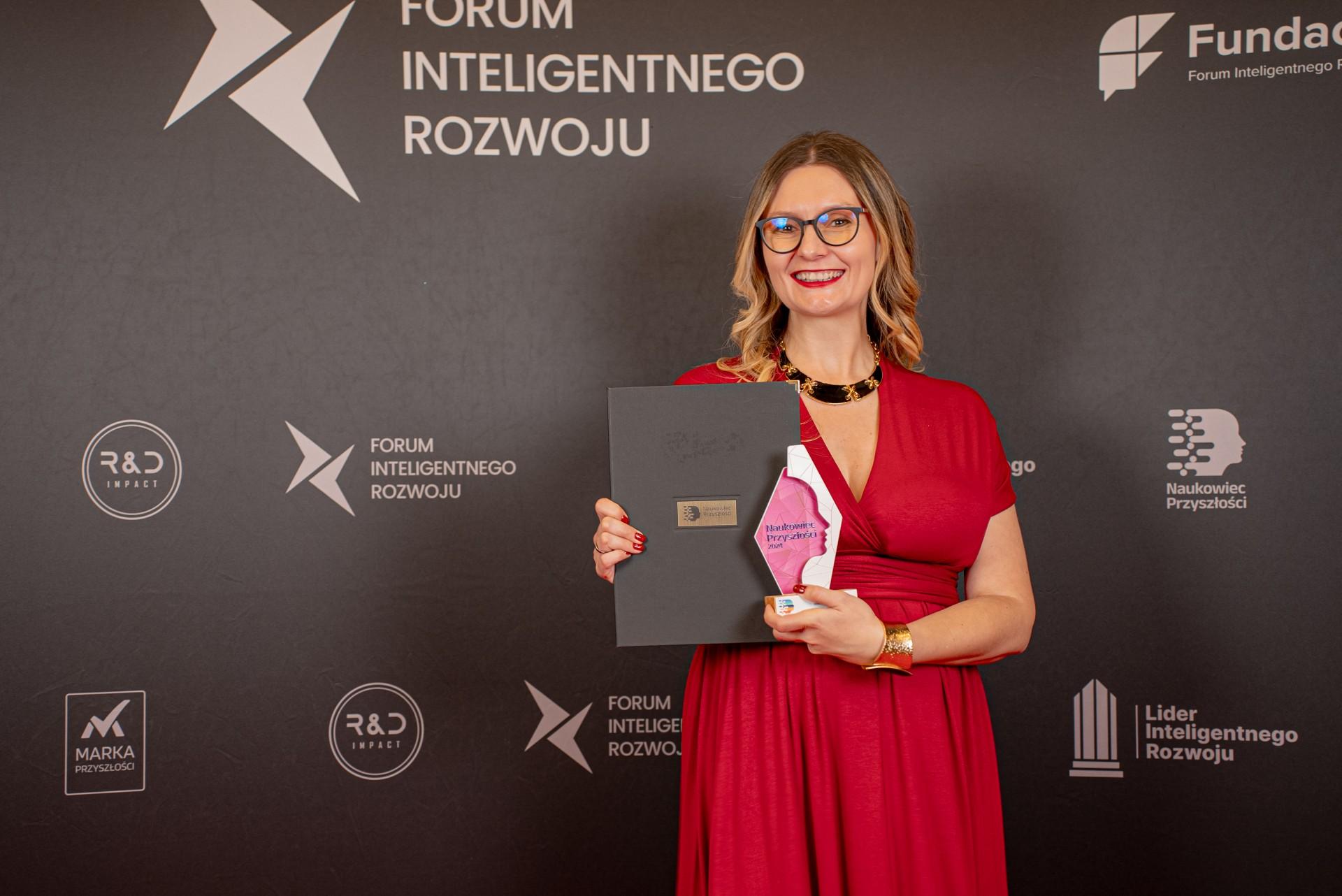 Dr Wróblewska stojąca ze statuetką na czerwonym dywanie, w tle widać ściankę z napisem Forum Inteligentnego Rozwoju