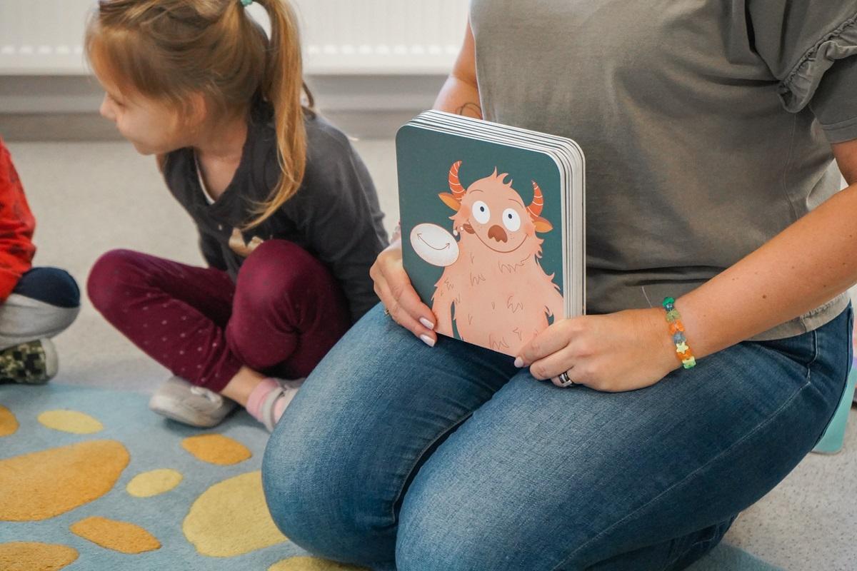 Nauczycielka trzyma na kolanach kolorowe karty edukacyjne